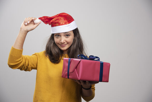 肖像戴着圣诞帽的微笑女人展示着一个礼品盒表情庆祝快乐