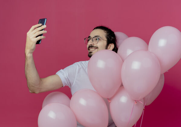 帅气笑容可掬的帅哥戴着眼镜捧着气球 孤身一人在粉红色上自拍抱着眼镜气球