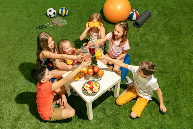 女孩儿童时尚概念一群十几岁的男孩和女孩坐在公园的绿色草地上果汁朋友童年