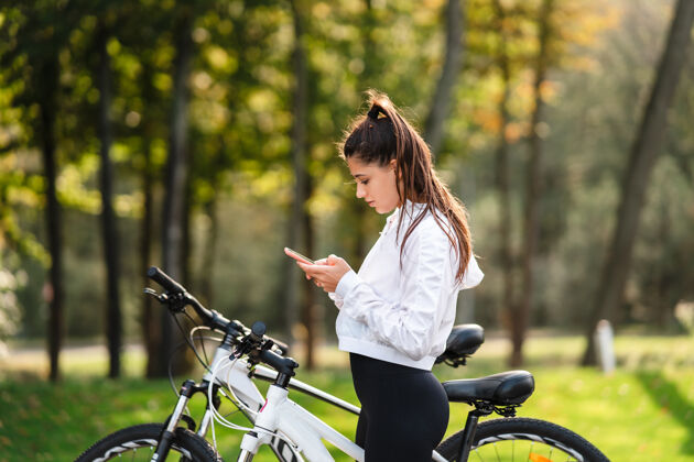 自行车在公园休息的年轻女子 在阳光明媚的天气里用手机女人活动电话