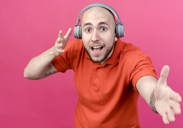 运动快乐的年轻人戴着耳机 伸出一只孤立的手站在粉红色的墙上男人年轻耳机
