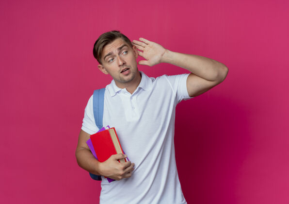 年轻看着身边年轻帅气的男同学背着书包拿着书 在粉红色的墙上表现出一种孤立的倾听姿态墙秀壁板