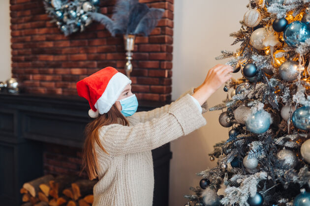 病毒一个年轻的女人用医用面具装饰圣诞树庆祝流行病树