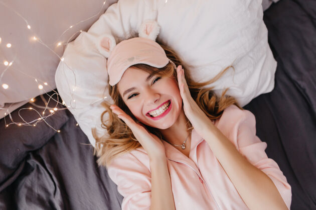 表情穿着粉色睡衣的迷人女孩躺在枕头上笑着可爱的金发女人在床上享受早晨的头像周末快乐床
