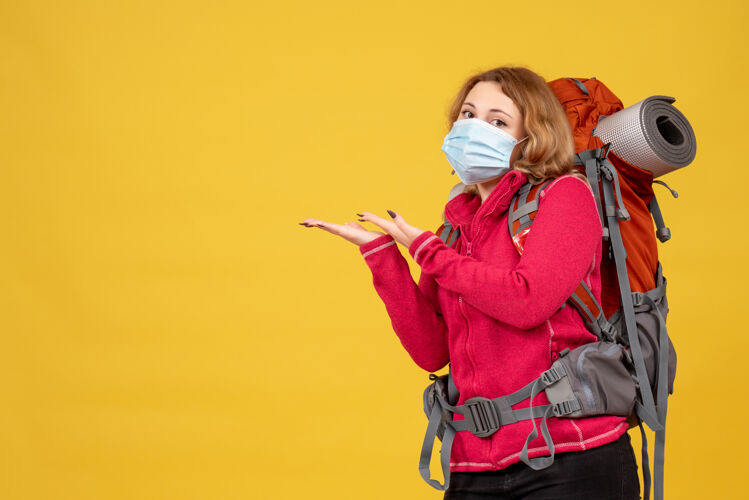 成人俯视图：戴着医用面罩的年轻旅行女孩正在收拾行李 并指向右边的东西指漂亮肖像