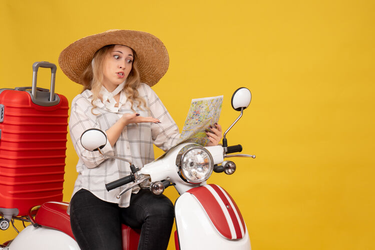 上衣顶视图好奇的年轻女子戴着帽子 坐在摩托车上 看着黄色的地图衣服肖像乐趣