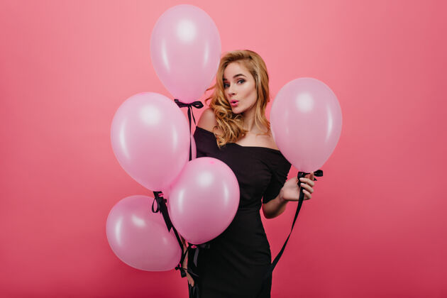气球优雅的白色气球女子摆出惊讶的表情迷人的卷发女孩等待生日派对的肖像粉色气球年轻美丽