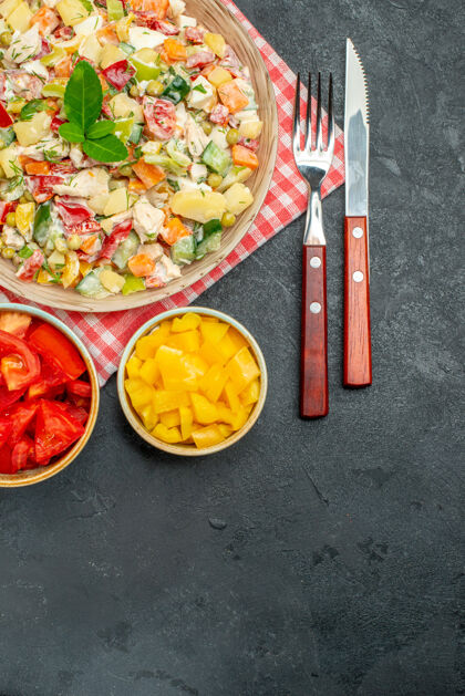 蔬菜红色餐巾上蔬菜沙拉碗的俯视图 蔬菜和餐具放在一边 黑色桌子底部有文本的自由空间地点餐巾午餐