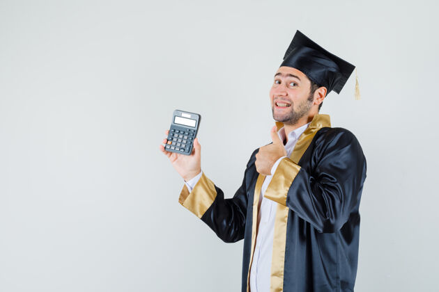 毕业年轻人拿着计算器 穿着研究生制服竖起大拇指 看上去很高兴正视图肖像男人英俊