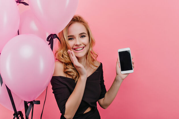 气球漂亮的女孩拿着新手机 面带微笑时髦的金发女人得到一个智能手机作为生日礼物优雅明亮庆祝