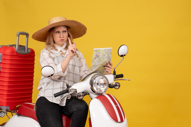 摩托车困惑的年轻女子戴着帽子 坐在摩托车上 拿着地图指着黄色人假日成人