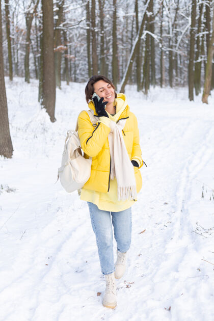 节日心情愉快的快乐女人漫步在雪域的冬日森林里 愉快地聊着电话 享受着公园里的户外时光女性微笑爱