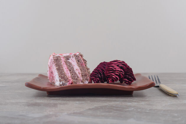 甜点一块蛋糕和红松球果放在一个盘子里 旁边是一个大理石叉子切片美味口感