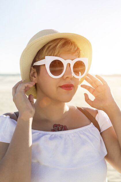 垂直一位戴着白色太阳镜和帽子的女性在海滩上的垂直镜头时尚放松优雅