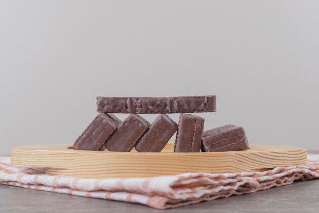 甜点把涂有巧克力的薄饼放在大理石上的木盘上美味外套巧克力