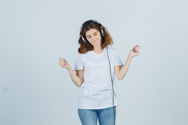 快乐穿着白色t恤 牛仔裤 戴着耳机欣赏音乐的年轻女性 看上去很活泼前视图模型销售漂亮