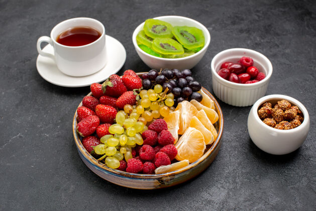 醇香的前视图水果组成不同的新鲜水果与茶在深灰色的桌子上早餐成分新鲜