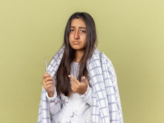 女孩悲伤的生病的年轻女孩裹着格子布 指着橄榄绿背景上孤立的温度计病年轻橄榄