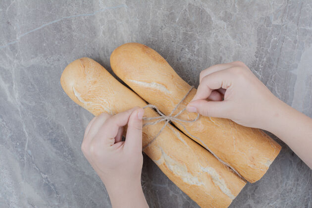 小吃手拿着半块法式面包放在大理石表面美味美味俯视图