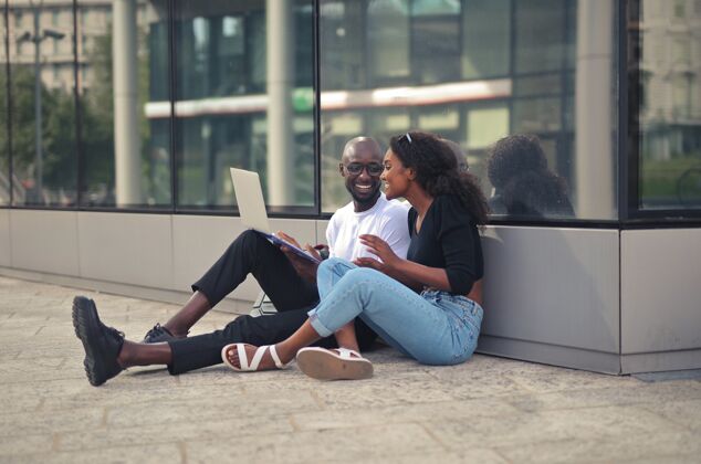 欢乐快乐微笑的非洲男女坐在地上 白天用笔记本电脑成人年轻街头