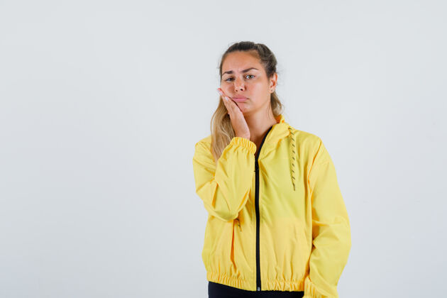 休闲穿着黄色雨衣的年轻女子抚摸着脸颊 看上去很痛苦雨衣脸厨房