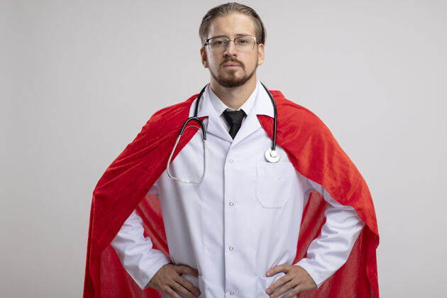 自信一个自信的年轻超级英雄 穿着医用长袍 戴着听诊器和眼镜 手放在臀部 背景是白色的臀部年轻人手