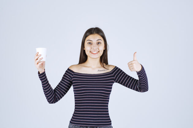 休闲穿着条纹衬衫的女孩拿着一个塑料咖啡杯 指着一个好味道女人成人人类