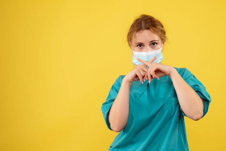 消毒黄色墙壁上穿着医疗服 戴着无菌口罩的年轻女医生的正视图人孩子可爱