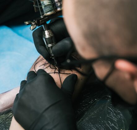 手选择性聚焦拍摄一个纹身艺术家与黑手套创造一个男人的手臂纹身绘画专业皮肤