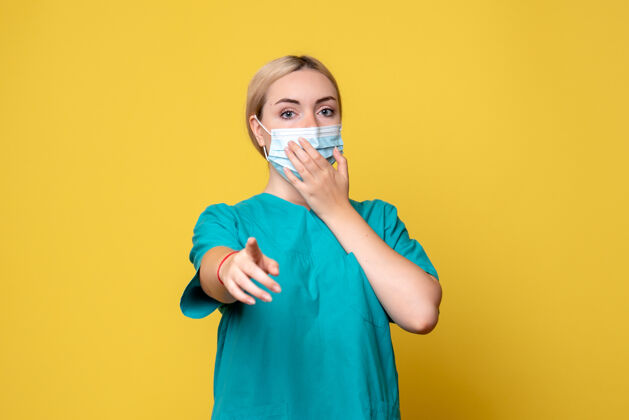 衬衫黄色墙上穿着医用衬衫和无菌口罩的年轻女医生的正视图年轻女医生大流行面具