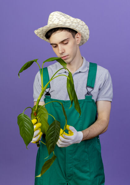 穿自信的年轻男性园丁戴着园艺帽和手套 手持植物手套男帽子