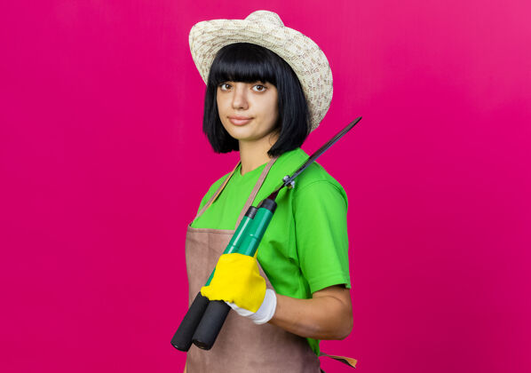 女自信的年轻女园丁穿着制服 戴着园艺帽 肩上扛着剪刀花园园艺粉红色