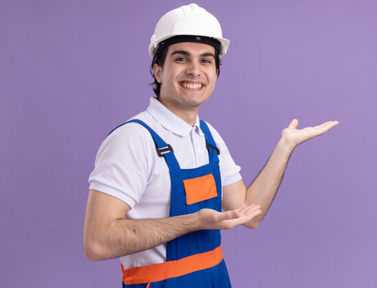 制服身穿施工制服 头戴安全帽的年轻建筑工人站在紫色的墙上 双臂望着前方 笑容满面安全大站立