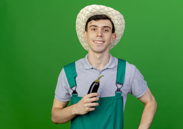 男性微笑的年轻男园丁戴着园艺帽捧着茄子绿色微笑举行