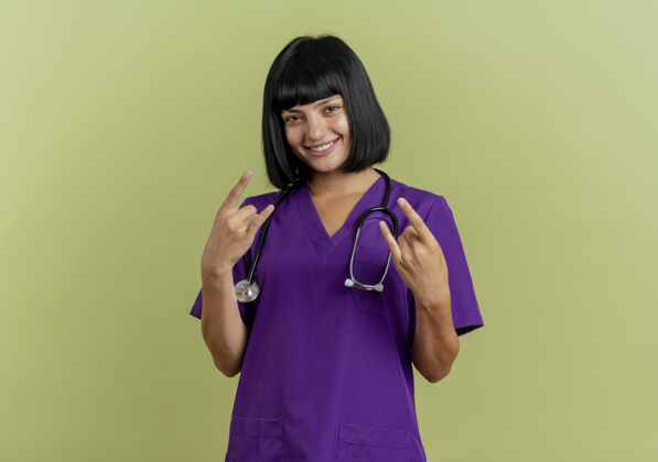复制微笑的年轻黑发女医生穿着制服用听诊器手势喇叭手势用两只手标志女性空间