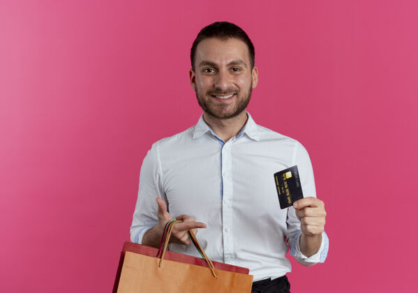纸笑容可掬的帅哥拿着纸购物袋和信用卡孤零零地贴在粉红色的墙上男人帅气优雅