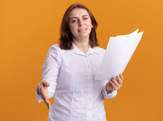 衬衫身穿白衬衫的年轻女子举着空白的书页伸出手望着前面微笑的问候站在橙色的墙上站着微笑页面