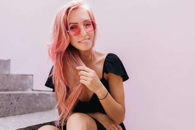 粉色头发性感的欧洲女模特一边在楼梯上放松一边抚摸着粉色的头发服饰享受年轻