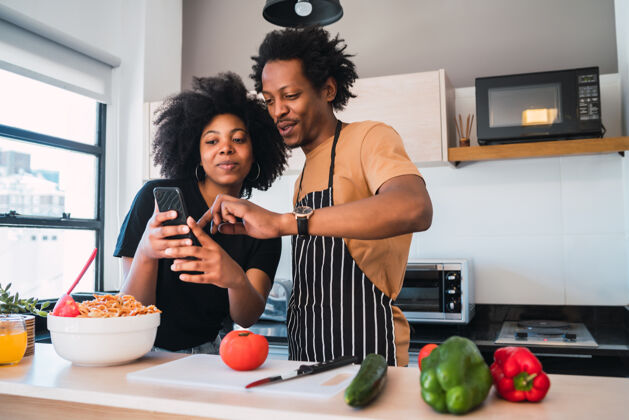女性一对年轻的非洲夫妇在家里的厨房里一起做饭和使用手机的照片欢呼食物美食