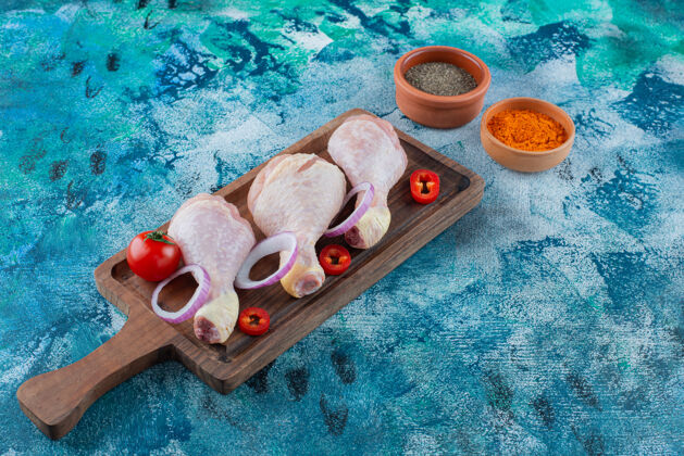 鸡腿生鸡腿和蔬菜放在一块板上 蓝色背景蛋白质生的蔬菜
