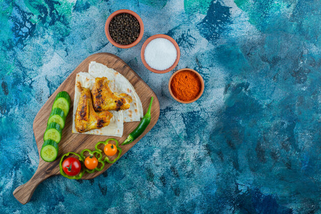 美味烤好的翅膀 拉瓦什和蔬菜放在砧板上 蓝色背景鸡翅胡椒美味