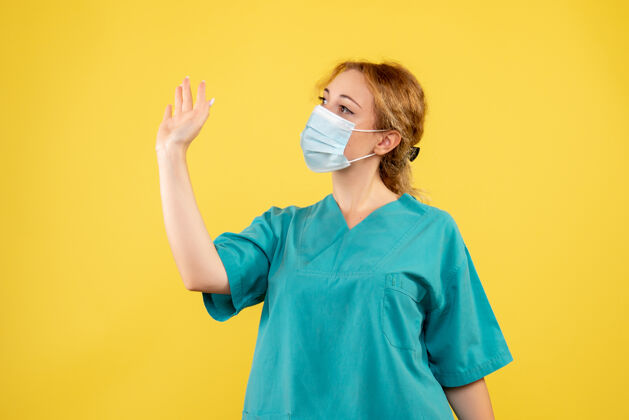 肖像黄色墙壁上穿着医疗服 戴着口罩的女医生的正视图家庭主妇套装流行病