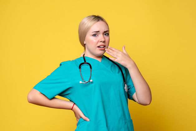 健康黄色墙上穿着带听诊器的医用衬衫的女医生的正视图听诊器护士病毒