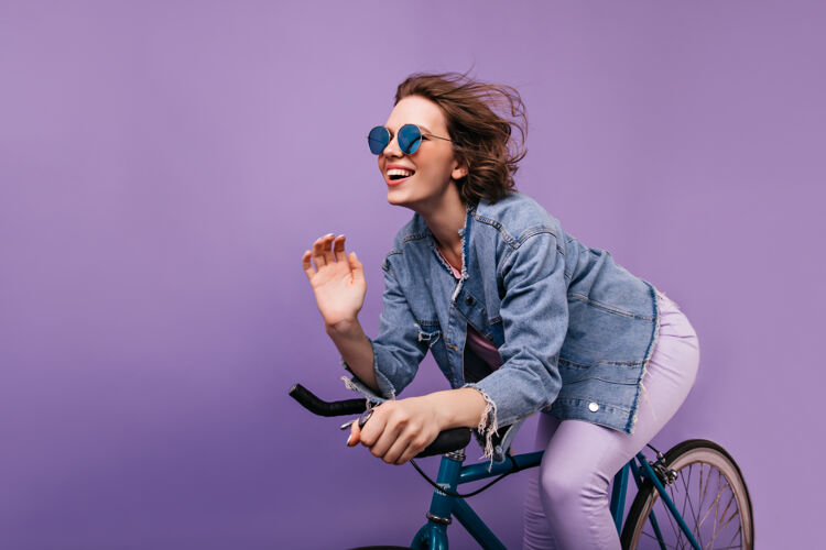 快乐幸福的女人穿着休闲夹克在自行车上摆姿势情绪化的短发女孩戴着闪闪发光的眼镜骑在自行车上放松年轻波浪发