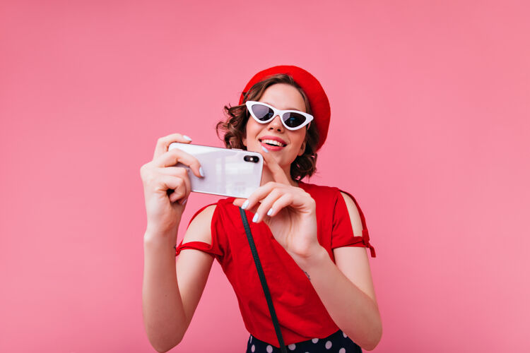 贝雷帽迷人的法国女士戴着复古眼镜在拍照卷曲的女士戴着红色贝雷帽在自拍年轻女性自拍