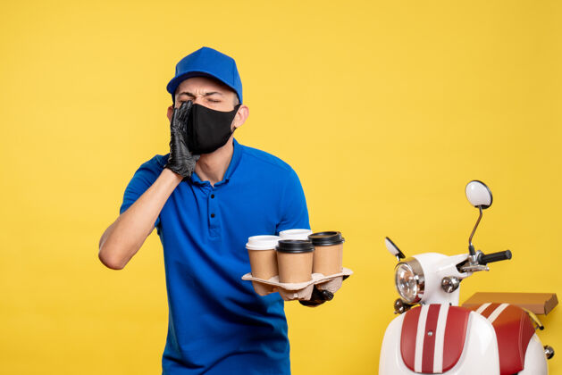 面具正面图戴口罩的男信使拿着咖啡在黄色工作服上-大流行服务递送制服工作视野男人咖啡