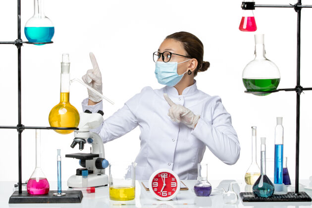 专业前视图穿着医疗服的女化学家带着面罩坐在白色背景上的溶液化学病毒-飞溅药物实验室病毒