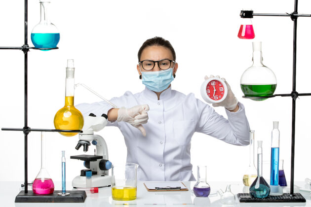 查看前视图：身穿医疗服的女化学家 戴着面具 白色背景上拿着红色的时钟病毒实验室化学冠状病毒-飞溅专业医生医学