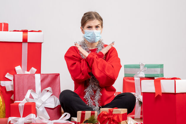 年正面图：年轻女性戴着无菌面具坐着 手里拿着圣诞礼物健康圣诞节面具