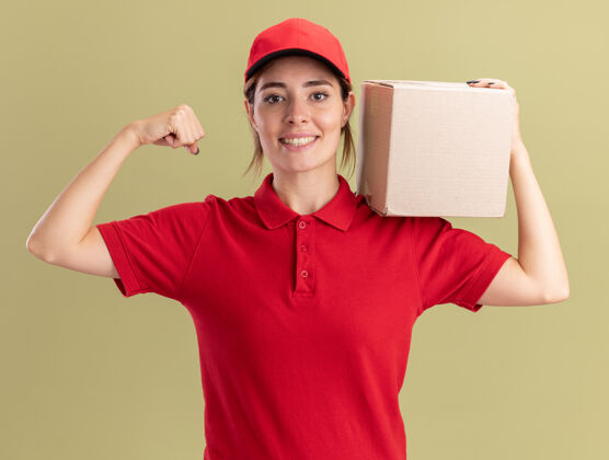 年轻微笑着的年轻漂亮的女送货员穿着制服拿着名片盒 紧绷着橄榄绿的二头肌姿势橄榄交货